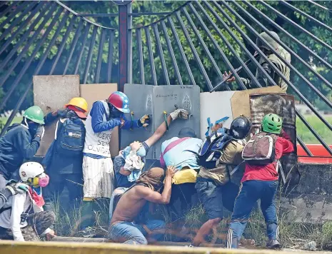  ?? (AFP) ?? Venezuelan opposition activists attempt to defilade behind a wall from a National Guard riot policeman shooting rubber bullets at them during clashes in Caracas in May this year