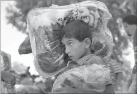  ?? LEFTERIS PITARAKIS/ THE ASSOCIATED PRESS ?? A Palestinia­n youth carries blankets donated to the U.N. school where hundreds of families sought refuge after fleeing their homes during missile strikes.