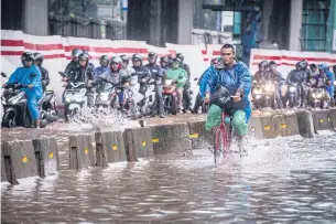  ?? REUTERS ?? A cyclist rides alongside motorcycli­sts along a flooded street in Jakarta yesterday.