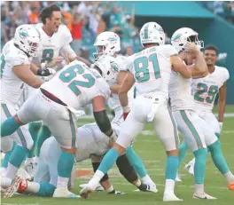  ?? AP ?? Dolphins kicker Jason Sanders (taking off helmet) is mobbed by teammates after making a 47-yard field goal to win the game as time expired in overtime.