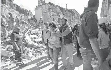  ?? ASSOCIATED PRESS ?? A woman is comforted as she walks through rubble after an earthquake, in Amatrice, central Italy, collapsing homes on top of residents as they slept. This town has the highest death toll with 224.