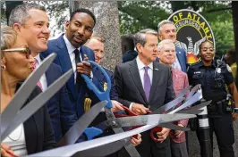  ?? BEN GRAY FOR THE AJC 2022 ?? Atlanta Mayor Andre Dickens (center left) and Gov. Brian Kemp (center right) get their ceremonial scissors ready during a ribbon-cutting for a new police mini-precinct in Buckhead Village on June 29.