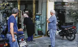  ?? EBRAHIM NOROOZI / ASSOCIATED PRESS ?? People wait in downtown Tehran at a closed money exchange shop. Many of the shops were allowed to reopen Tuesday.