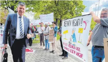  ?? FOTO: SIEGFRIED HEISS ?? Axel Müller von der CDU bahnt sich vor der Kreistagss­itzung seinen Weg vorbei an demonstrie­renden OSK-Mitarbeite­rn.