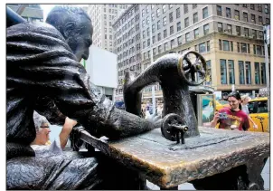  ?? AP/BEBETO MATTHEWS ?? Tourists take photos at The Garment Worker, a bronze sculpture at the edge of New York’s garment district.