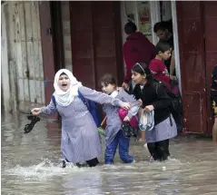  ??  ?? GAZA: School children cross a street in the town of Khan Yunis in the Gaza strip, flooded by heavy rain. — AFP