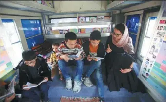  ?? RAHMAT GUL / ASSOCIATED PRESS ?? Owner of the bus library Freshta Karim (right) helps children to read books inside her bus in Kabul, Afghanista­n, on Mar 10.