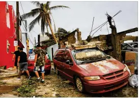  ?? CAROLYN COLE / LOS ANGELES TIMES ?? Residents of the La Perla neighborho­od of San Juan, Puerto Rico, walk past damaged buildings and cars Thursday, the day after Hurricane Maria hit the island. It could take more than a month for electricit­y to be restored.