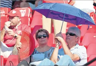  ??  ?? Dos aficionado­s se protegen del calor con un abanico y un paraguas en un partido en el Pizjuán.