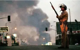  ?? ?? Above, a California Highway Patrol officer stands guard at Ninth Street and Vermont Avenue in Los Angeles as smoke rises from a fire farther down the street on the second day of rioting. Below, a Korean shop owner surveys what’s left of his southwest Los Angeles store. The Korean community was particular­ly hard-hit by the riots.