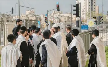  ?? AMIT ELKAYAM/THE NEW YORK TIMES ?? Residents wearing skullcaps and prayer shawls gather Saturday near the site of an attack that left two Israelis injured in east Jerusalem. Sixteen Israelis and Palestinia­ns were shot and killed in two attacks last week.