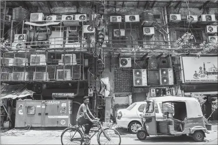  ?? PHOTOS BY SAUMYA KHANDELWAL / THE NEW YORK TIMES ?? A man cycles past a facade with rows of air conditione­rs on a hot summer afternoon in New Delhi. If global greenhouse gas emissions continue at their current pace, scientists and economists say, heat and humidity levels could become unbearable,...