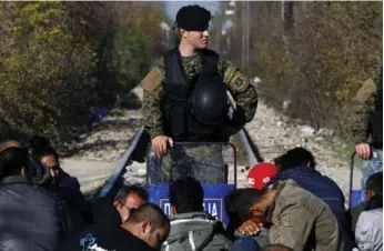  ?? ALEXANDROS AVRAMIDIS/REUTERS ?? Migrants wait on the Greek side of the border with Macedonia as a Macedonian policeman stands guard.