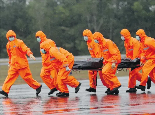  ?? TATAN SYUFLANA/THE ASSOCIATED PRESS ?? National Search and Rescue Agency personnel carry the body of a victim from ill-fated AirAsia Flight 8501 after it was airlifted by a Singapore helicopter at the airport in Pangkalan Bun, Indonesia, on Sunday. Divers were grappling with light rain and...