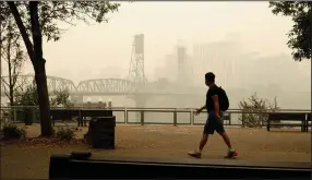  ?? (AP/Don Ryan) ?? A man walks near the Willamette Bridge in downtown Portland, Ore., on Wednesday as smoke from wildfires continues to cloud the area.