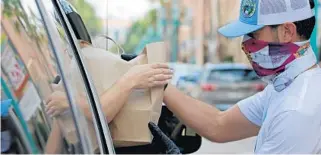  ?? JOHN MCCALL/SOUTH FLORIDA SUN SENTINEL ?? Boca Raton City Council member Andy Thomson delivers food to a driver during a grocery distributi­on event organized by Hospitalit­y Helping Hands to help workers in April 2020.