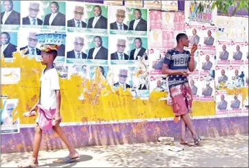  ?? — AFP photo ?? A man stands next to campaign posters in Freetown, while the results of the country’s general elections are still awaited, three days after the vote.