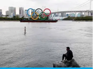  ?? — AFP ?? TOKYO: A man sits on a rock in front of the Olympic rings at the Odaiba waterfront in Tokyo on Monday.