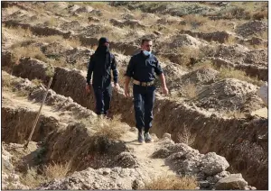  ?? AP ?? Syrian workers for a human-rights group walk through the site believed to be a mass grave containing the bodies of hundreds of people near Raqqa in northern Syria.
