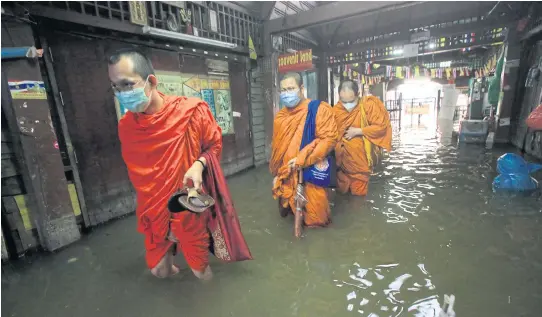  ?? PORNPROM SATRABHAYA ?? Monks wade through floodwater by Tha Tien pier along the Chao Phraya River. The National Water Command Centre and the Thai Meteorolog­ical Department have estimated the water level of the river will rise by 20cm-40cm.