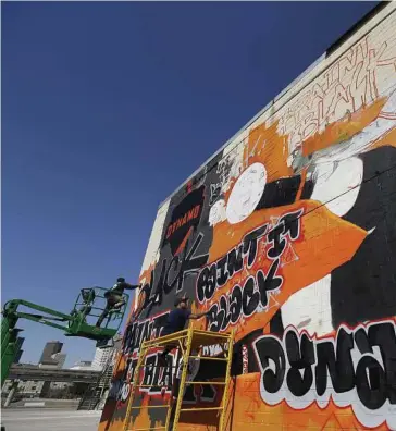  ??  ?? Mario Figueroa, left, and Jojo Villarreal paint a Dynamo art mural featuring the new black jersey at the corner of Leeland and Chartres.