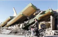  ??  ?? A motorcycli­st rides by a damaged building in Darbandikh­an, Kurdistan