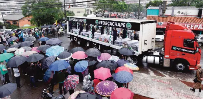  ?? —AFP ?? CHAPECO: People attend under heavy rain the passage of the funeral cortege with the coffins of the members of the Chapecoens­e Real football club team killed in a plane crash in Colombia.