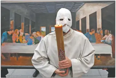  ?? (AP/Petr David Josek) ?? A participan­t wearing a mask holds a candle as he stands in front of a depiction of the painting the Last Supper.