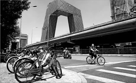  ?? SHIRLEY FENG/WASHINGTON POST ?? A cyclist rides an Ofo bike past other dockless bikes in Beijing, where the low-cost rental service is immensely popular.