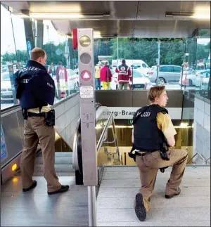  ?? AP/LUKAS SCHULZE ?? German police officers keep a lookout Friday at a subway station near a Munich shopping mall where a gunman opened fire. The gunman’s whereabout­s were not known until later in the evening.