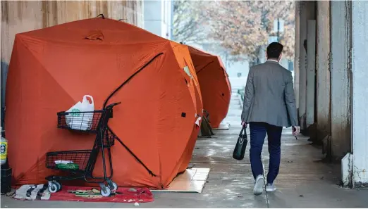  ?? PAT NABONG/SUN-TIMES ?? A person in a suit walks past tents occupied by homeless people under a viaduct in the West Loop in November.