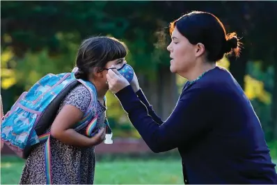  ?? The Associated Press ?? ■ Sarah Staffiere adjusts a face covering on her daughter, Natalie, before school Thursday in Waterville, Maine. Staffiere, a senior laboratory instructor at Colby College, said she will be relieved when her two children can be vaccinated.