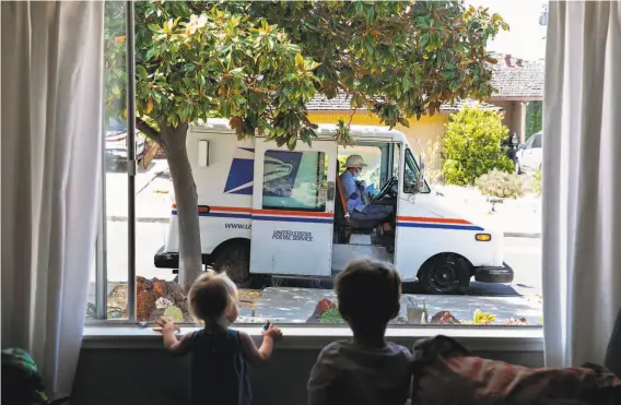  ?? Jessica Christian / The Chronicle ?? In May, siblings Leila, 1, and Liam HavenarDau­ghton, 3, watch a postal carrier in front of their home in El Sobrante, where they have been sheltering in place.