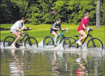  ?? Jason Fochtman
The Associated Press ?? Children ride their bikes through rising floodwater­s near Lake Houston on Saturday.