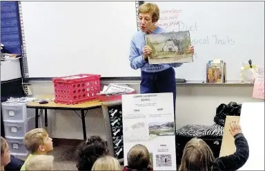  ?? Lynn Atkins/Weekly Vista ?? Xyta Lucas, president of the Bella Vista Historical Society, displays to a class of second graders at Cooper Elementary School a watercolor depicting the riding stable that was once on the land that later became the school.