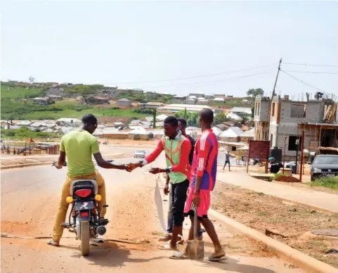  ?? Photo Ikechukwu Ibe ?? Youths filling potholes on a road at Kpebbi village junction, Asokoro Extension, collect a tip from a cyclist yesterday.