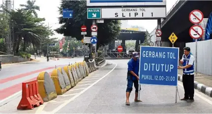  ?? — The Jakarta Post/ANN ?? Tight squeeze on traffic: Officials putting up a sign that bars vehicles from entering the Slipi 1 tollgate in West Jakarta.