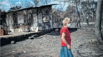  ?? ANGELOS TZORTZINIS/AFP/GETTY IMAGES ?? A woman wearing a mask walks in front of her burned house following a wildfire at the village of Neos Voutzas, near Athens.
