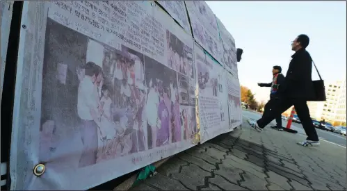  ?? (File Photo/AP/Ahn Young-joon) ?? People walk April 2, 2019, past a photo of guards unloading children from a truck at the Brothers Home in Busan as the image is displayed in front of the National Assembly in Seoul, South Korea.