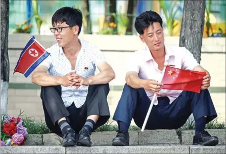  ?? ED JONES/AFP ?? Two men sit holding North Korean and Chinese flags near Kim Il-sung square in Pyongyang on Thursday, as Chinese President Xi Jinping visits the country.