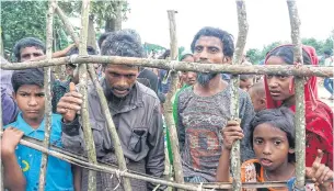  ??  ?? Newly-arrived Rohingya refugees standing behind a wooden fence at Kutupalong refugee camp in Ukhiya after crossing the border from Myanmar into Bangladesh on Tuesday.