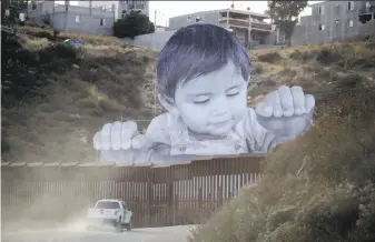  ?? Gregory Bull / Associated Press ?? A Border Patrol vehicle passes a mural of a boy peering over the barrier wall in Tecate (San Diego County). The image is the work of French artist JR and stands 65 feet tall.