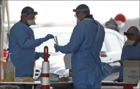  ?? KATHY WILLENS — THE ASSOCIATED PRESS ?? A worker pulls a COVID-19 bottle out of a kit as another worker helps him Wednesday, March 18, at a New York State Department of Health drive-through testing facility at Jones Beach State Park in Wantagh on Long Island.