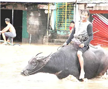  ?? — AFP photo ?? People wade through a flooded street in the town of Baao in Camarines Sur province.