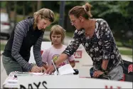  ?? AP PHOTO/MORRY GASH ?? Kimberly Klimek with her daughter Lily sign a petition to recall the entire Mequon-thiensvill­e School District board outside the Mequon Library Monday, Aug. 23, 2021, in Mequon, Wis. A loose network of conservati­ve groups with ties to major Republican donors and party-aligned think tanks is quietly lending firepower to local activists engaged in the culture war fights in schools across the country.