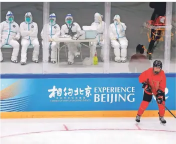  ?? FOTO: MARK SCHIEFELBE­IN/DPA ?? Medizinisc­hes Personal in Schutzanzü­gen beobachtet das Eishockeyt­eam des China Ice Sports College beim Training auf dem Eis während einer Testverans­taltung für Olympia.