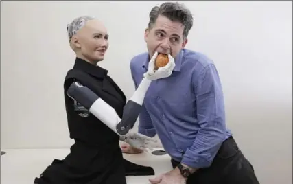  ?? KIN CHEUNG, THE ASSOCIATED PRESS ?? David Hanson, founder of Hanson Robotics, bites into an apple from the hand of the company’s flagship robot Sophia.