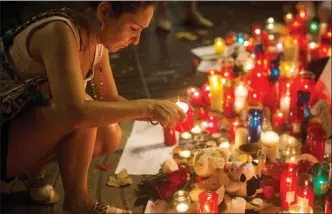  ?? The Associated Press ?? A woman lights up a candle at a memorial tribute to the victims of the vehicle attacks on Barcelona’s historic Las Ramblas promenade in Barcelona, Spain, on Sunday.