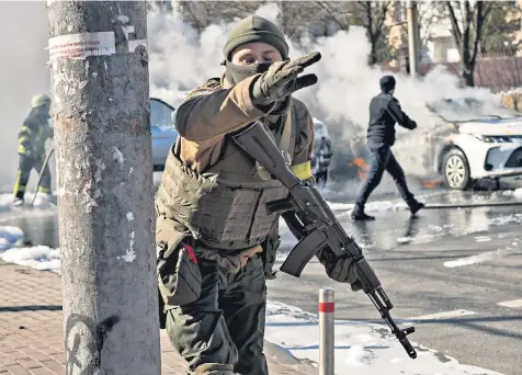  ?? ?? Ukrainian soldiers take positions outside a military facility as two cars burn in a street in Kyiv yesterday