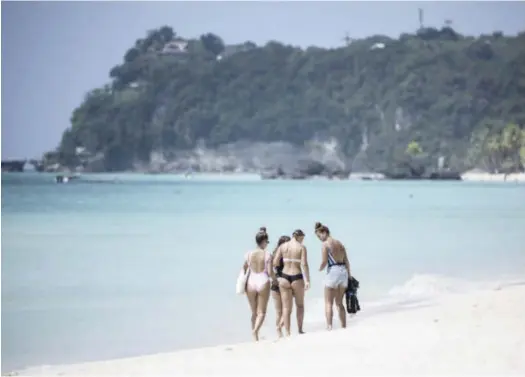  ?? AFP ?? Tourists walk along a rehabilita­ted beach in Boracay Island, a day after the popular tourist destinatio­n reopened in late October, to welcome tourists landing by boatloads on the resort island.